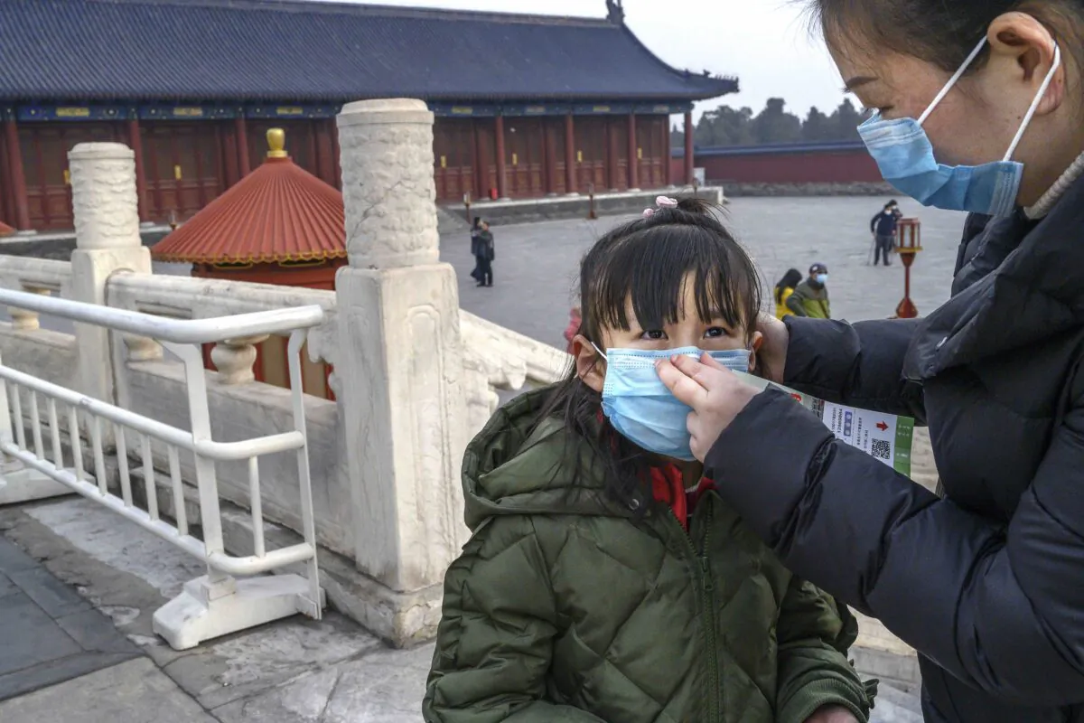 A Chinese woman puts a protective mask on a young girl as they tour the grounds of the Temple of Heaven in Beijing, China, which remained open during the Chinese New Year and Spring Festival holiday on Jan. 27, 2020. (Kevin Frayer/Getty Images)