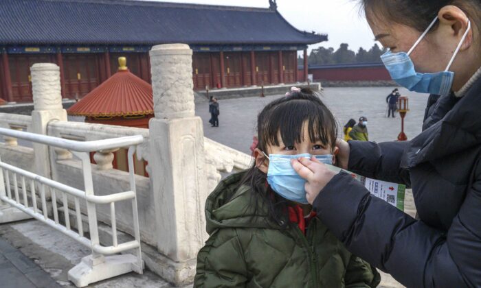 A Chinese woman puts a protective mask on a young girl as they tour the grounds of the Temple of Heaven in Beijing, China, which remained open during the Chinese New Year and Spring Festival holiday on Jan. 27, 2020. (Kevin Frayer/Getty Images)