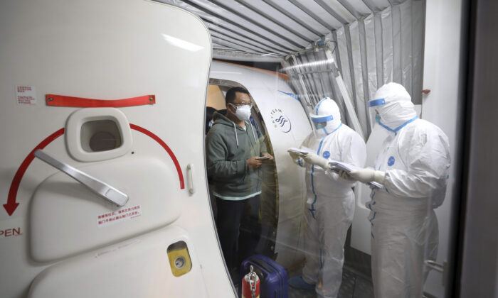 Quarantine workers in protective suits check identity documents as tourists from the Wuhan area walk off of a chartered plane taking them home from Bangkok at Wuhan Tianhe International Airport in Wuhan, Hubei Province, on Jan. 31, 2020. (Chinatopix via AP)