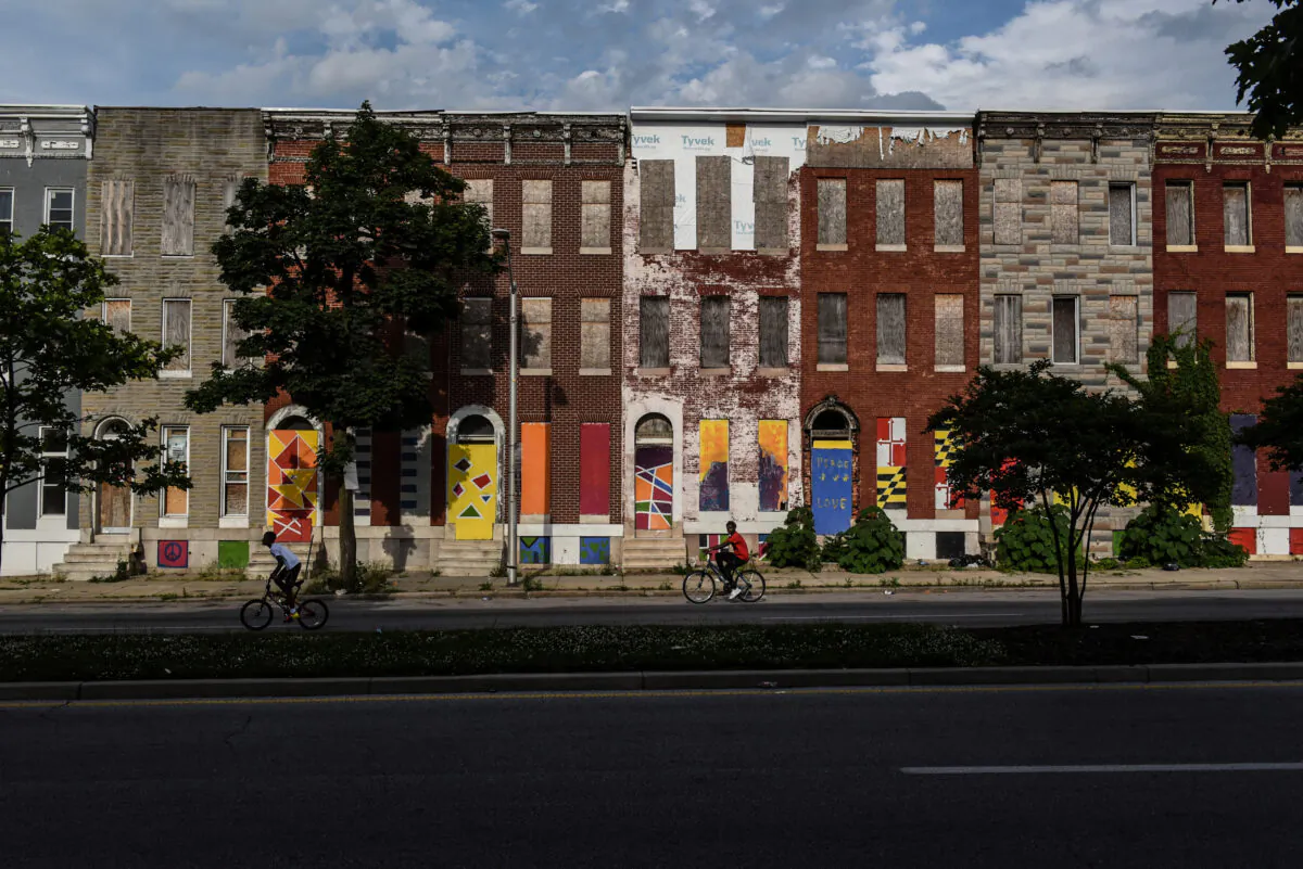 Young boys ride their bikes past boarded-up and abandoned row of houses in Baltimore, Md., on May 26, 2019. (Stephanie Keith/Reuters)