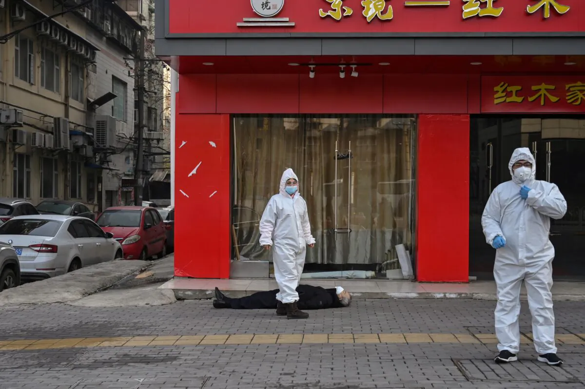 Chinese officials in protective suits checking on an elderly man wearing a facemask who collapsed and died on a street near a hospital in Wuhan, China, on Jan. 30, 2020. (Hector Retamal/AFP via Getty Images)