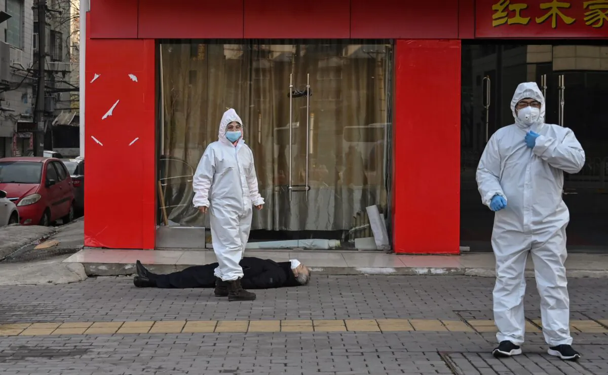 Chinese officials in protective suits checking on an elderly man wearing a facemask who collapsed and died on a street near a hospital in Wuhan, China, on Jan. 30, 2020. (HECTOR RETAMAL/AFP via Getty Images)