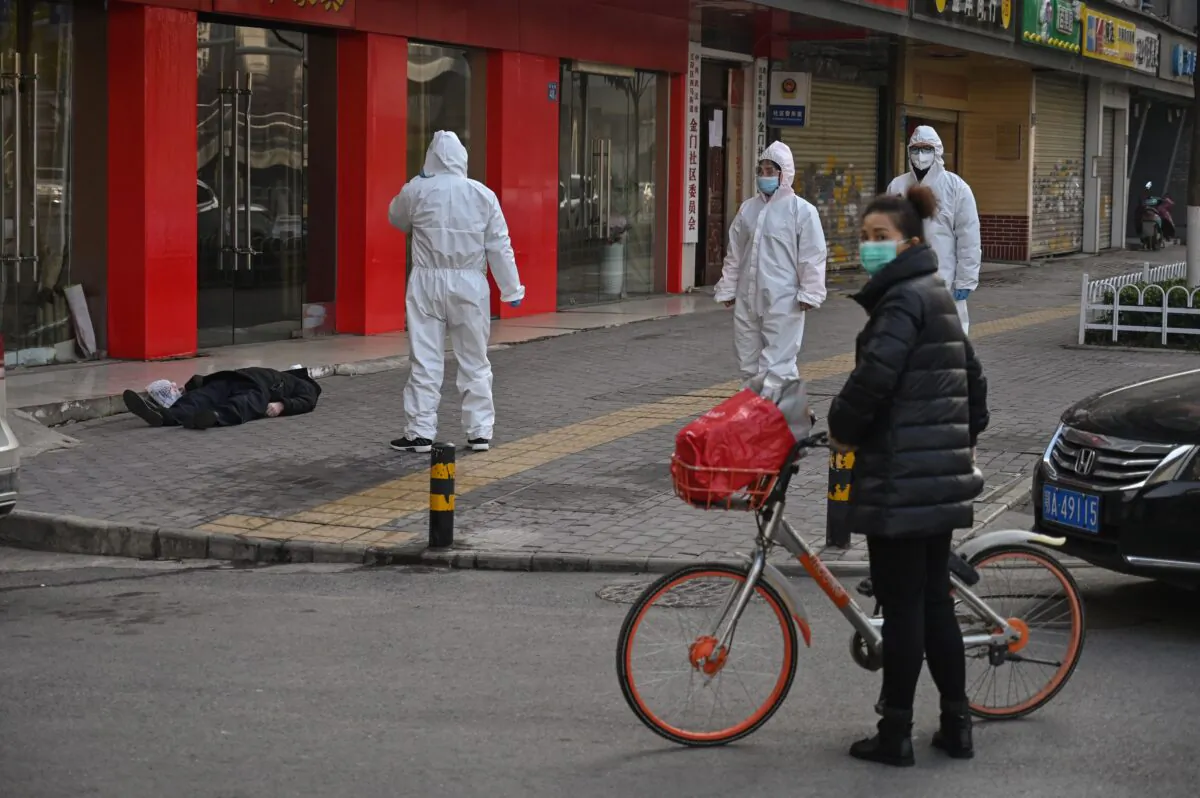 Chinese officials in protective suits checking on an elderly man wearing a face mask who collapsed and died on a street near a hospital in Wuhan, China, on Jan. 30, 2020. AFP journalists saw the body not long before an emergency vehicle arrived carrying police and medical staff in full-body protective suits. (Hector Retamal/AFP via Getty Images)
