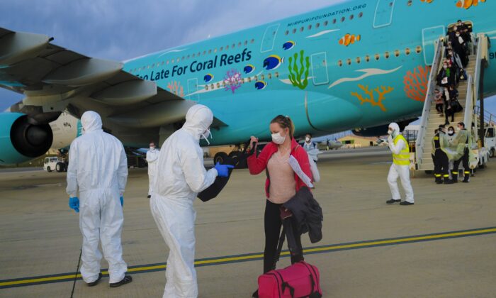A worker wearing a protective suit checks the luggage of an evacuee from Wuhan, China, after their evacuation flight landed at an airport in Marseilles, France, on Feb. 2, 2020. (AP Photo/Arek Rataj)