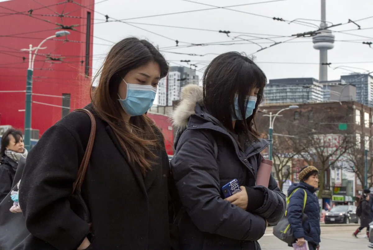 Pedestrians wear protective masks as they walk in Toronto on Jan. 27, 2020. Parents and other primary caregivers will accompany their Canadian children back to Canada after leaving Wuhan, the epicentre of an outbreak of the novel coronavirus, even if they are not citizens themselves. (The Canadian Press/Frank Gunn)
