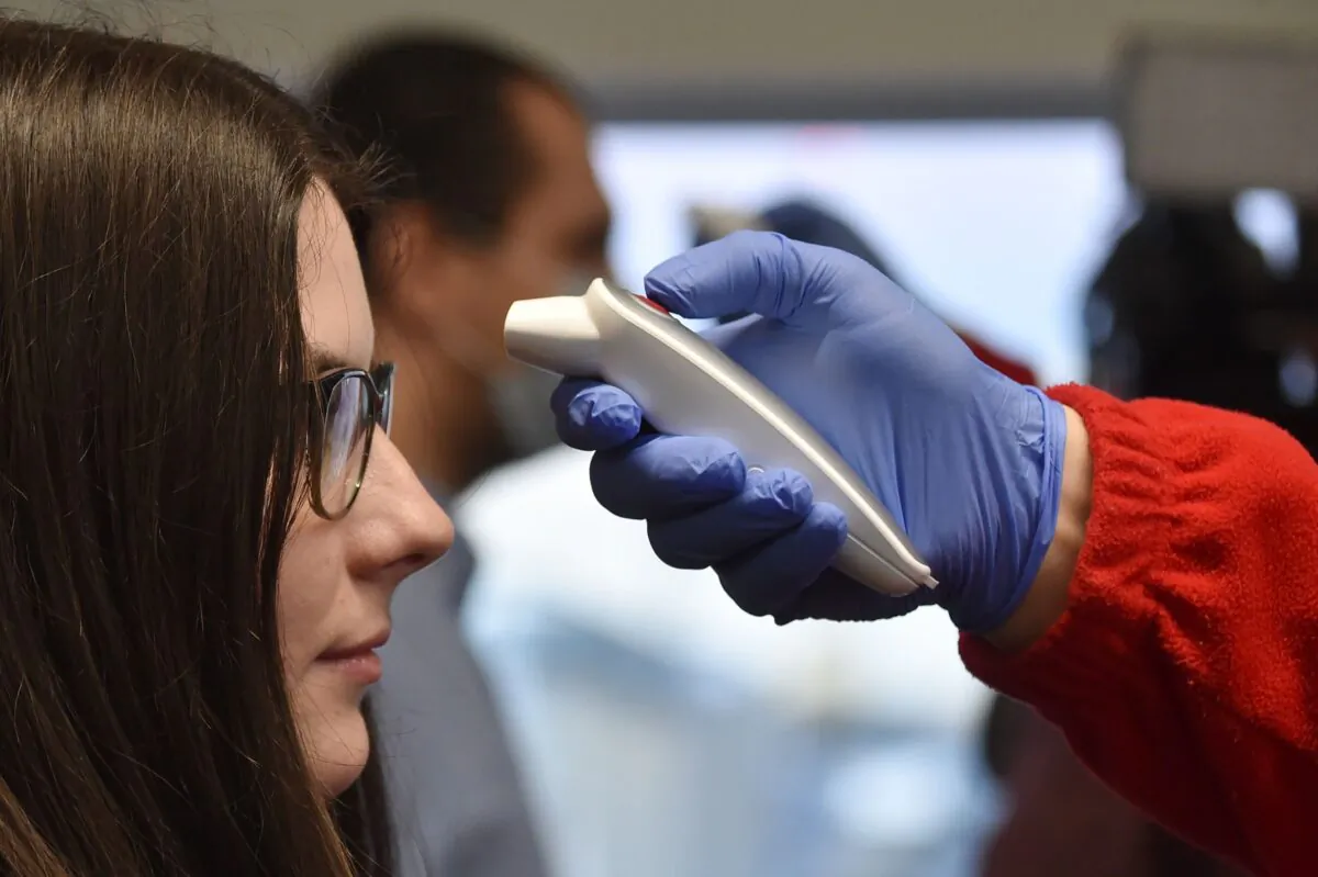 Member of the Airport Medical Service takes a temperature reading from staff members with a digital thermometer at Budapest's Liszt Ferenc Airport on Feb. 5, 2020. (Attila Kisbenedek/AFP via Getty Images)