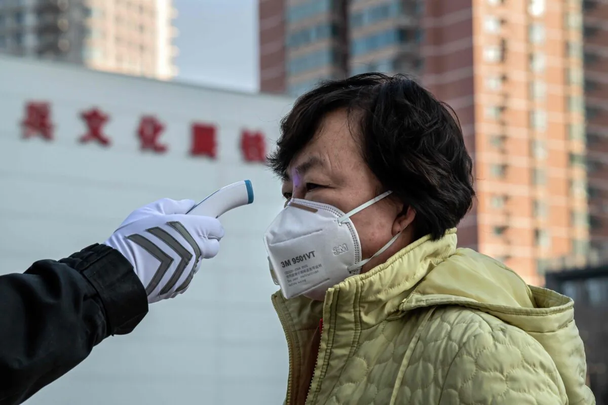 A security guard checks the temperature of a woman wearing a protective mask at the entrance of a park in Beijing, China on Jan. 31, 2020. (NICOLAS ASFOURI/AFP via Getty Images)