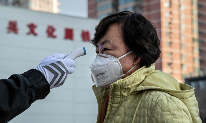 A security guard checks the temperature of a woman wearing a protective mask at the entrance of a park in Beijing, China on Jan. 31, 2020. (NICOLAS ASFOURI/AFP via Getty Images)