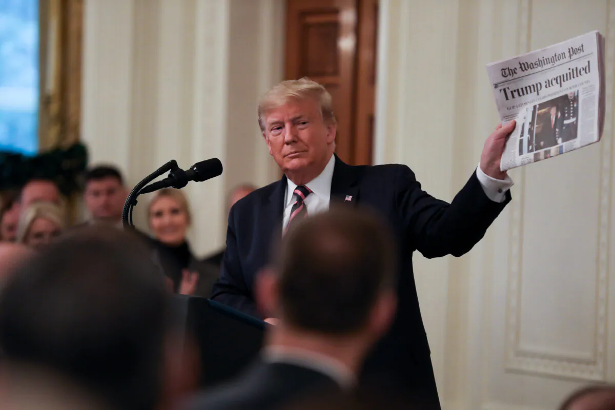 President Donald Trump holds up a newspaper during his victory speech a day after being acquitted on two articles of impeachment, in the East Room of the White House on Feb. 6, 2020. (Charlotte Cuthbertson/The Epoch Times)