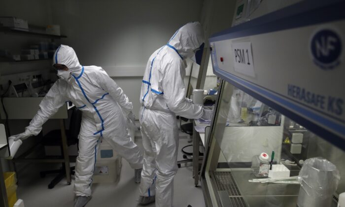 French lab scientists in hazmat gear inserting liquid in test tube manipulate potentially infected patient samples at Pasteur Institute in Paris on Feb. 6, 2020. (Francois Mori/AP Photo)