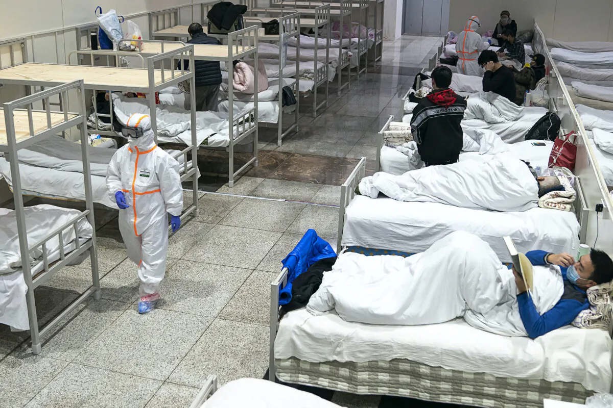 Medical worker in protective suit walks by patients diagnosed with the coronaviruses in a temporary hospital transformed from an exhibition center in Wuhan in central China's Hubei province on Feb. 5, 2020. (Chinatopix via AP)