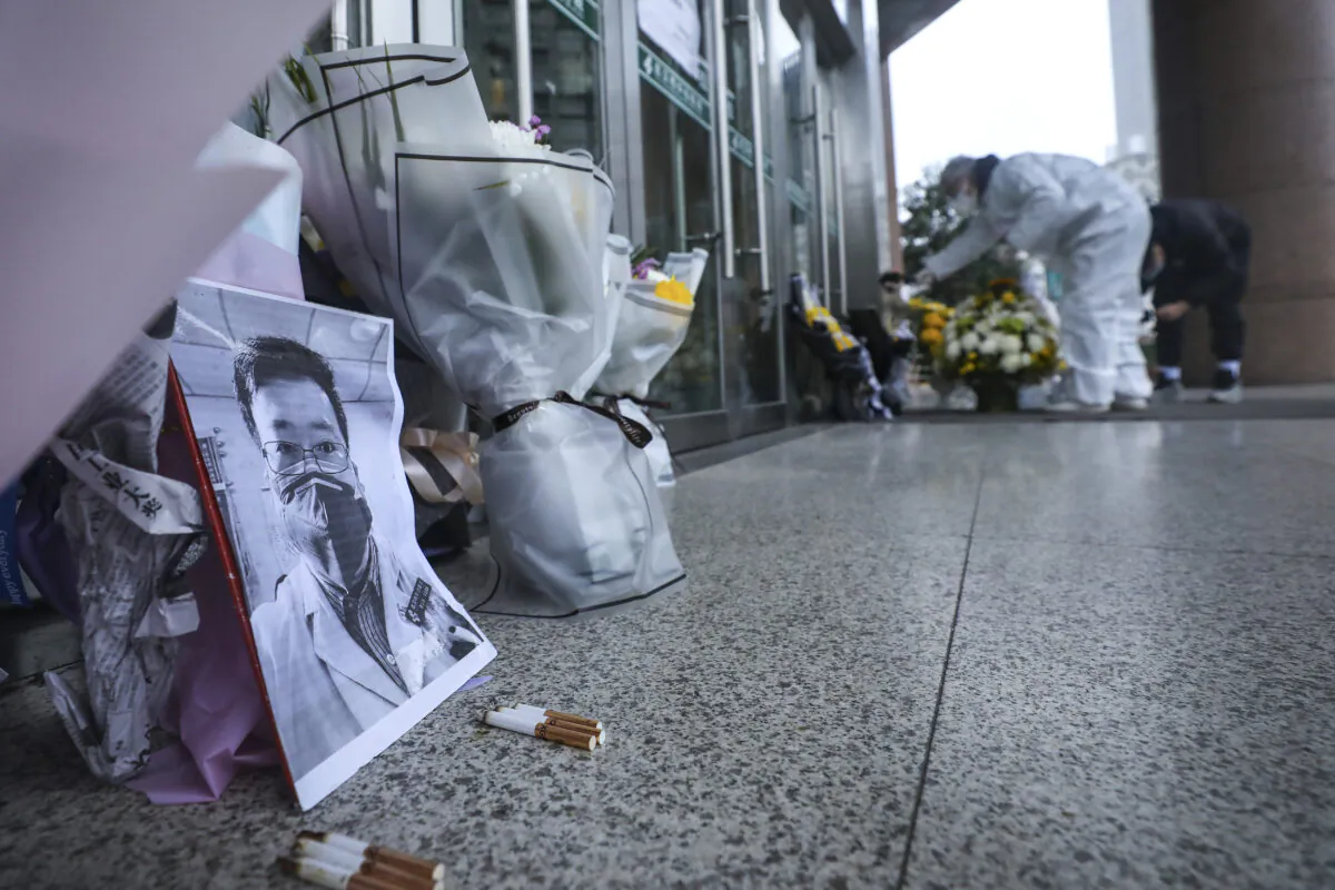 People pay condolence in front of flowers lying near a photo of the late Dr. Li Wenliang at a hospital in Wuhan in central China's Hubei Province, on Feb. 7, 2020. The death of the doctor who was reprimanded for warning about China's new virus triggered an outpouring on Friday of praise for him and fury that communist authorities put politics above public safety. In death. (Chinatopix via AP)