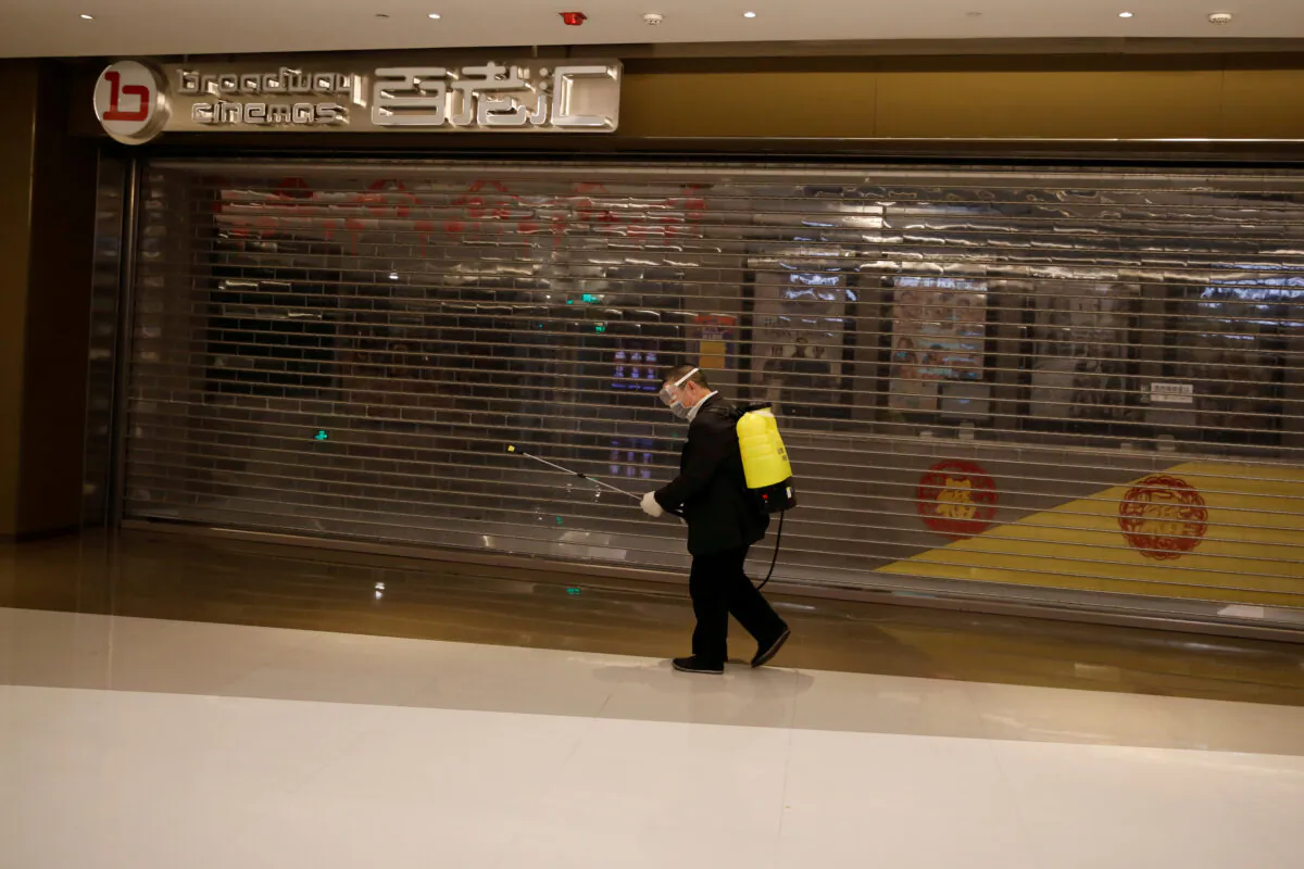 A staff member carrying sanitizing equipment walks past a closed cinema at a shopping mall, as the country is hit by the outbreak of the new coronavirus, in Beijing, China on Feb. 3, 2020. (Carlos Garcia Rawlins/Reuters)