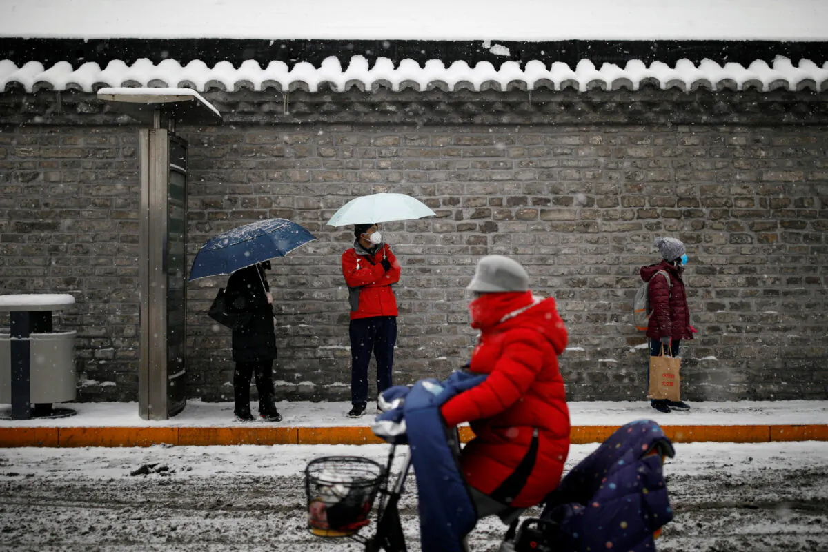 People wearing masks wait amid snow at a bus stop as the country is hit by an outbreak of the novel coronavirus, in Beijing, China on Feb. 6, 2020. (Carlos Garcia Rawlins/Reuters)