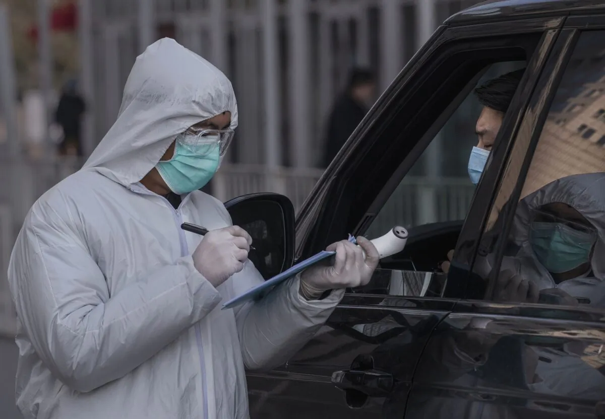 A Chinese worker wears a protective suit as he takes the name of a driver in a vehicle entering an office building while checking people in Beijing on Feb. 10, 2020. (Kevin Frayer/Getty Images)