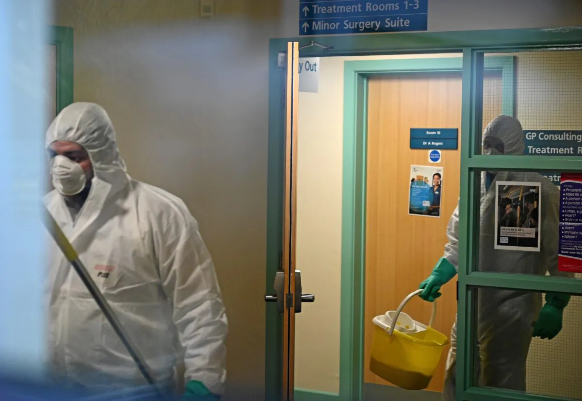 Workers dressed in protective clothing, including face masks and gloves, are pictured carrying buckets as they work inside Warmdene doctor's surgery at County Oak Medical Center in Brighton, United Kingdom, after it closed following reports a member of staff was infected with the Novel Coronavirus, on Feb. 10, 2020. (Glyn Kirk//AFP via Getty Images)
