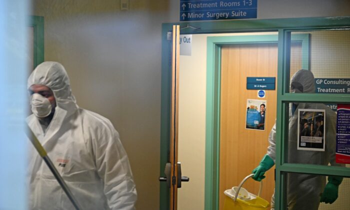 Workers dressed in protective clothing, including face masks and gloves, are pictured carrying buckets as they work inside Warmdene doctor's surgery at County Oak Medical Center in Brighton, United Kingdom, after it closed following reports a member of staff was infected with the Novel Coronavirus, on Feb. 10, 2020. (Glyn Kirk//AFP via Getty Images)