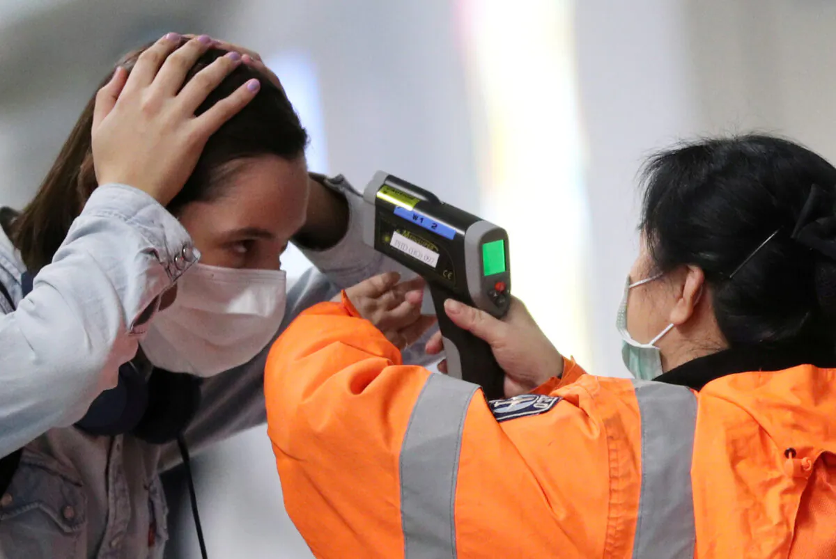 A worker checks the temperature of a passenger arriving into Hong Kong International Airport with an infrared thermometer, following the coronavirus outbreak in Hong Kong, China, on Feb. 7, 2020. (Hannah McKay/Reuters)