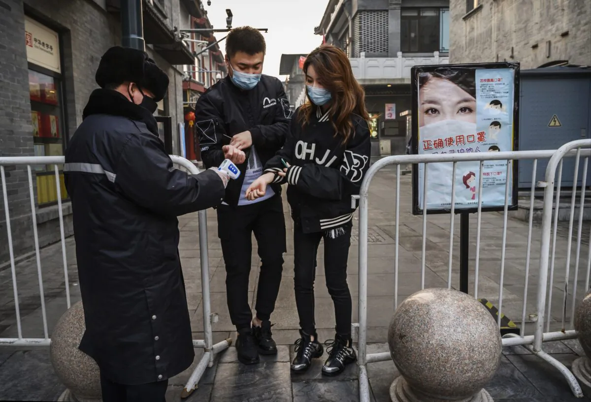 A Chinese security guard takes the temperature of a couple as they enter a nearly empty commercial street in Beijing, China, on Feb. 12, 2020. (Kevin Frayer/Getty Images)