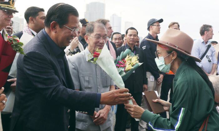 Cambodia's Prime Minister Hun Sen, left, gives a bouquet of flowers to a passenger who disembarked from the MS Westerdam, owned by Holland America Line, at the port of Sihanoukville, Cambodia, Friday, Feb. 14, 2020. (Heng Sinith/AP)

