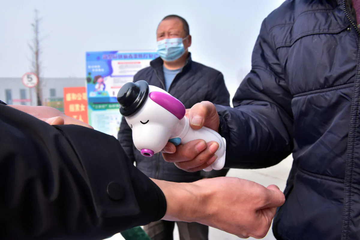 A guard measures the body temperature of a worker with a thermometer at the entrance to a factory, as the country is hit by an outbreak of the novel coronavirus, in Shijiazhuang, Hebei Province, China on Feb. 13, 2020. (China Daily via Reuters)