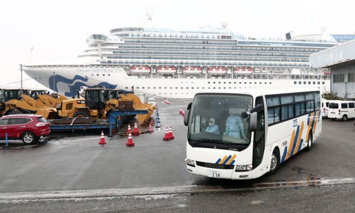 A bus with a driver (L) wearing protective gear departs from the dockside next to the Diamond Princess cruise ship, at the Daikoku Pier Cruise Terminal in Yokohama port in Japan on Feb. 16, 2020. (Behrouz Mehri/AFP via Getty Images)