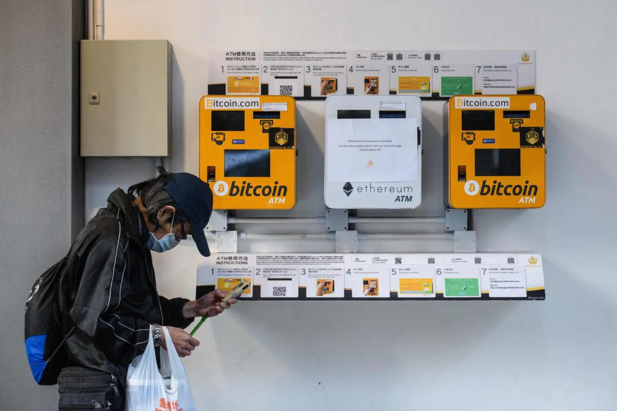 A man uses his phone as he walks past ATM machines for digital currency Bitcoin in Hong Kong on Dec. 18, 2017. (Anthony Wallace/AFP via Getty Images)