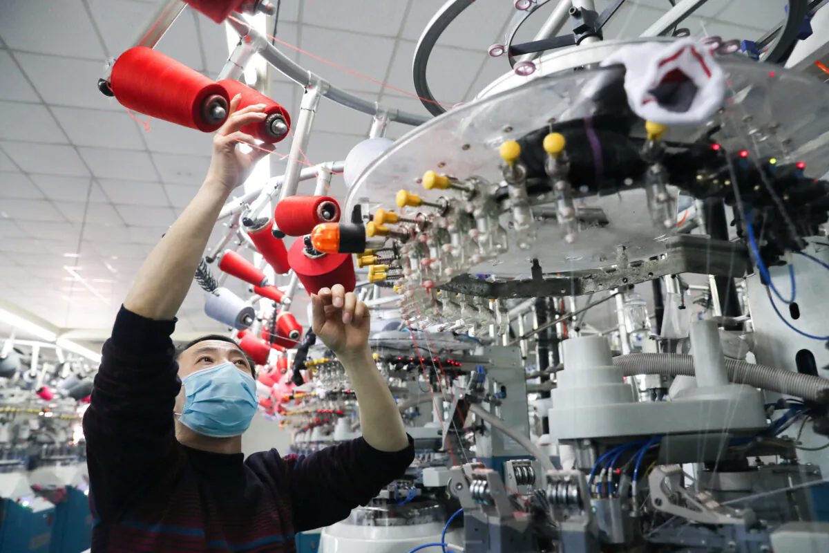 An employee wearing a face mask works on a production line manufacturing socks for export at a factory in Huzhou's Deqing County, Zhejiang Province, China on Feb. 19, 2020. (China Daily via Reuters)