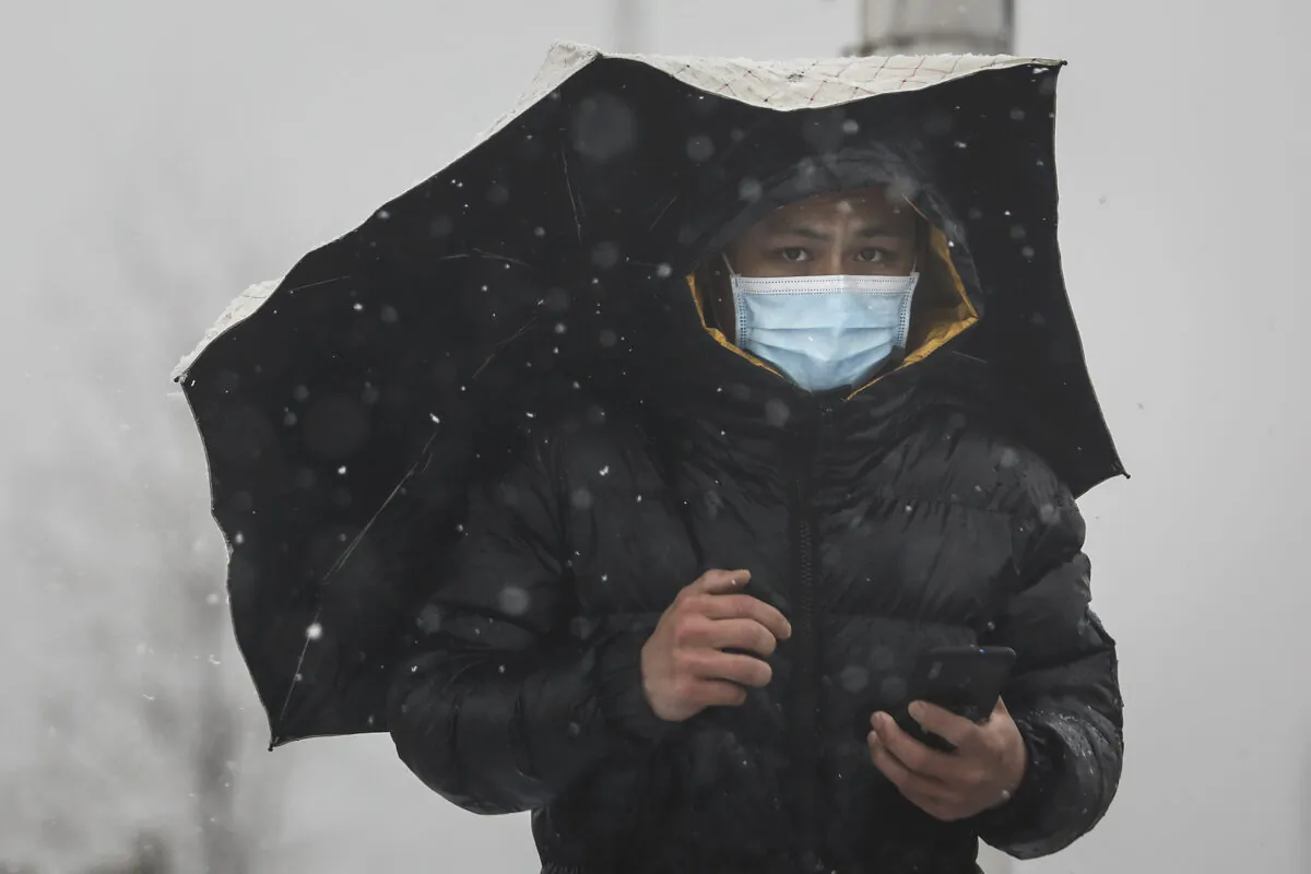 A man wears a protective mask as he holds an umbrella on the Yangzi river bridge as snow falls in Wuhan, Hubei, China, on Feb. 15, 2020. (Getty Images)