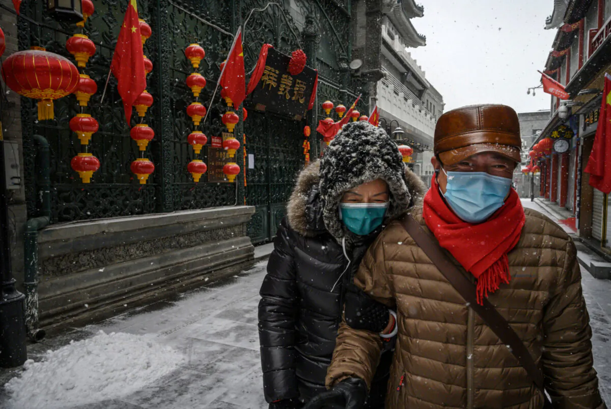 A Chinese couple wear protective masks as they walk during a snowfall in an empty and shuttered commercial street in Beijing, China, on Feb. 5, 2020. (Kevin Frayer/Getty Images)