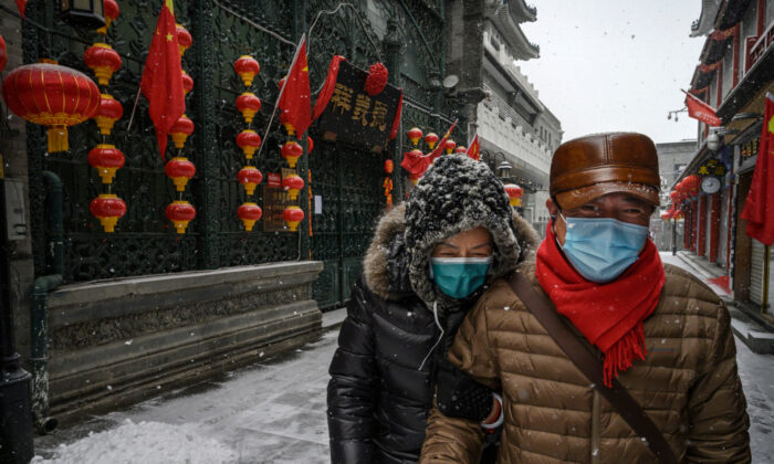 A Chinese couple wear protective masks as they walk during a snowfall in an empty and shuttered commercial street in Beijing, China, on Feb. 5, 2020. (Kevin Frayer/Getty Images)