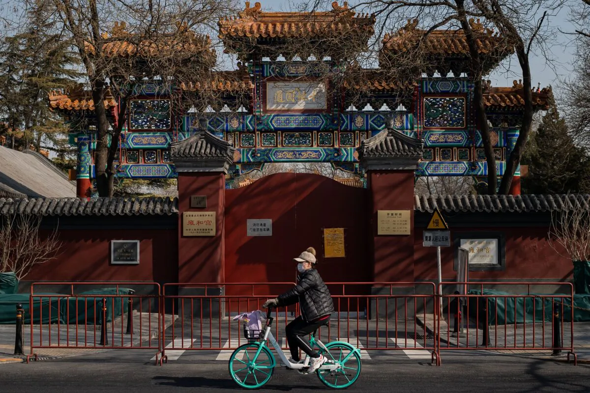 A woman wearing a protective facemask to protect against the COVID-19 coronavirus cycles in front of the Lama Temple in Beijing, China on Feb. 23, 2020. (NICOLAS ASFOURI/AFP via Getty Images)