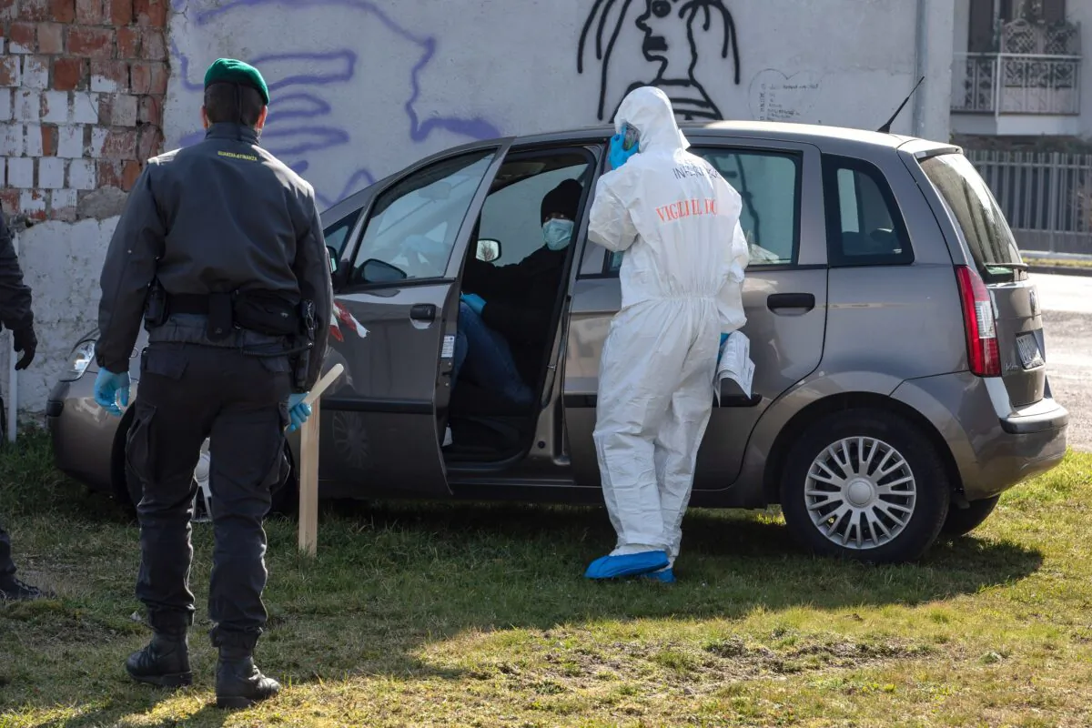 A rescue worker, wearing a protective suit, checks the medical conditions of a man who tried to reach a hospital driving his own car but was eventually stopped by Italian Guardia di Finanza (Custom Police) officers at a road block in Casalpusterlengo, Italy, on Feb. 24, 2020. (Emanuele Cremaschi/Getty Images)