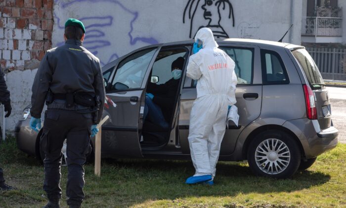 A rescue worker, wearing a protective suit, checks the medical conditions of a man who tried to reach a hospital driving his own car but was eventually stopped by Italian Guardia di Finanza (Custom Police) officers at a road block in Casalpusterlengo, Italy, on Feb. 24, 2020. (Emanuele Cremaschi/Getty Images)