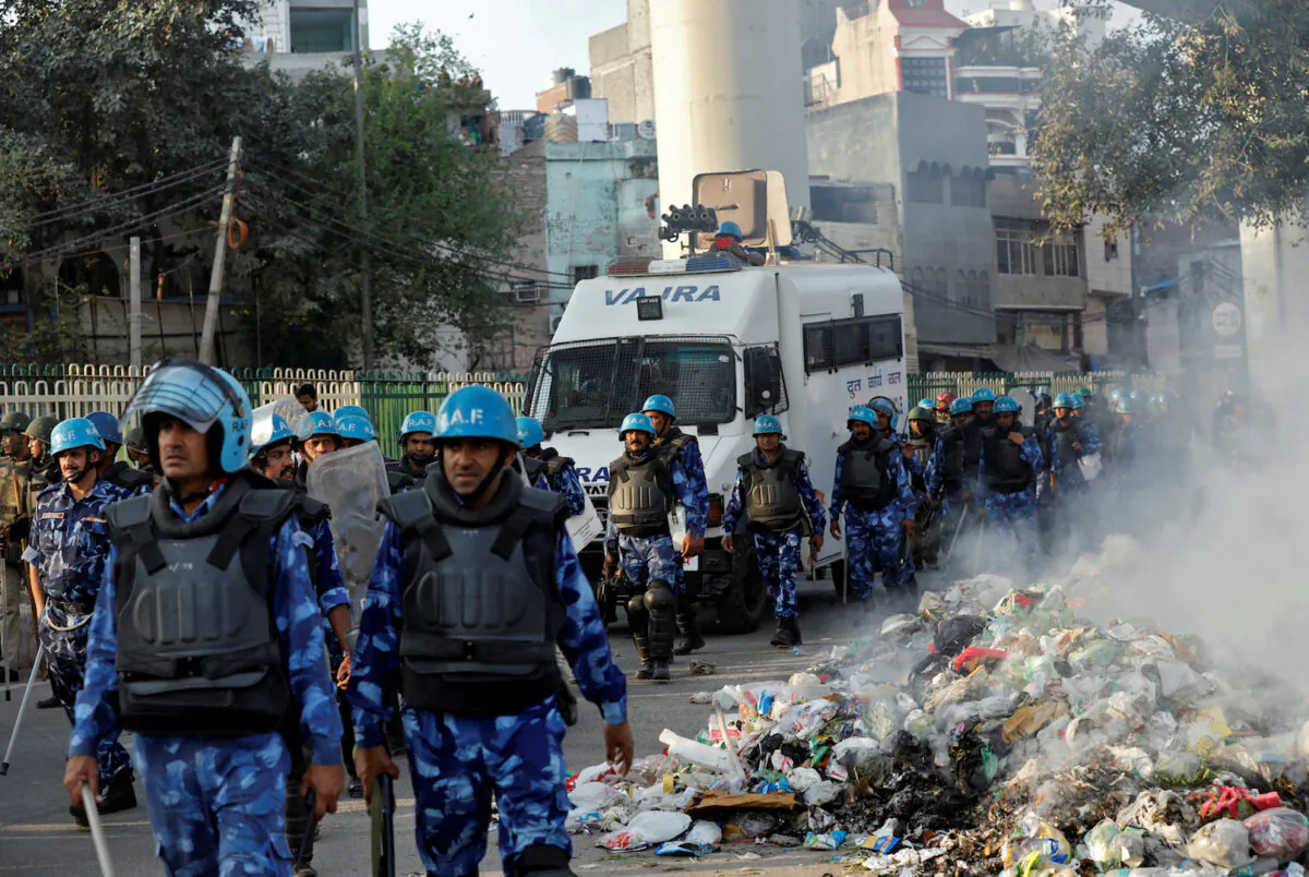 Members of Rapid Action Force move past smoldering debris after it was set on fire by demonstrators in New Delhi, India, on Feb. 25, 2020. (Danish Siddiqui/Reuters)
