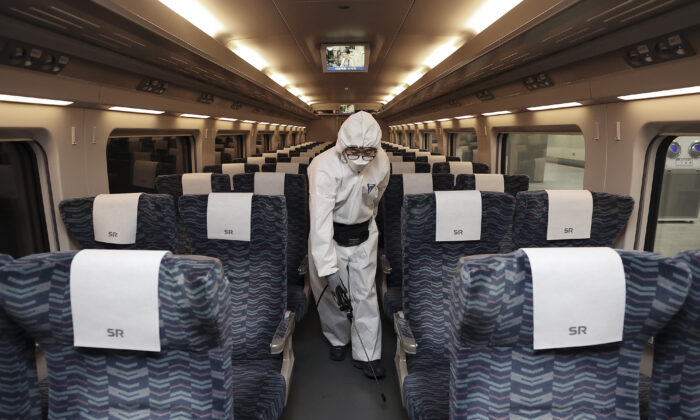 A worker wearing protective gears sprays disinfectant as a precaution on a train against the new coronavirus at Suseo Railway Station in Seoul on Feb. 25, 2020. (Lee Ji-eun/Yonhap via AP)