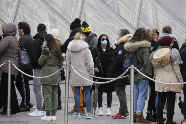Tourists, some wearing a mask, queue to enter the Louvre museum