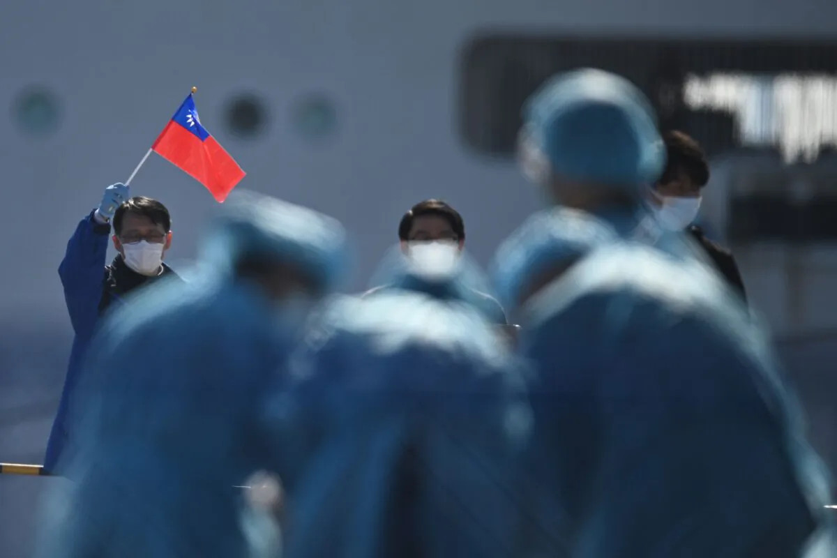 A man (L) holds a Taiwan flag as passengers disembark from the Diamond Princess cruise ship, in quarantine due to fears of new COVID-19 coronavirus, at the Daikoku pier cruise terminal in Yokohama on Feb. 21, 2020. (Philip Fong/AFP via Getty Images)