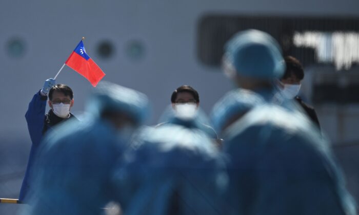 A man (L) holds a Taiwan flag as passengers disembark from the Diamond Princess cruise ship, in quarantine due to fears of new COVID-19 coronavirus, at the Daikoku pier cruise terminal in Yokohama on Feb. 21, 2020. (Philip Fong/AFP via Getty Images)