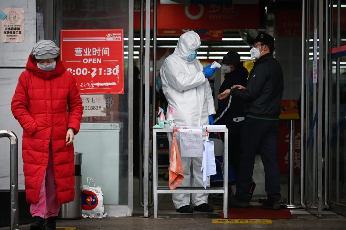 A staff member of a supermarket wearing a protective suit uses a thermometer to check the temperature of customers at the entrance of a supermarket in Beijing on Feb. 29, 2020. (STR/AFP via Getty Images)