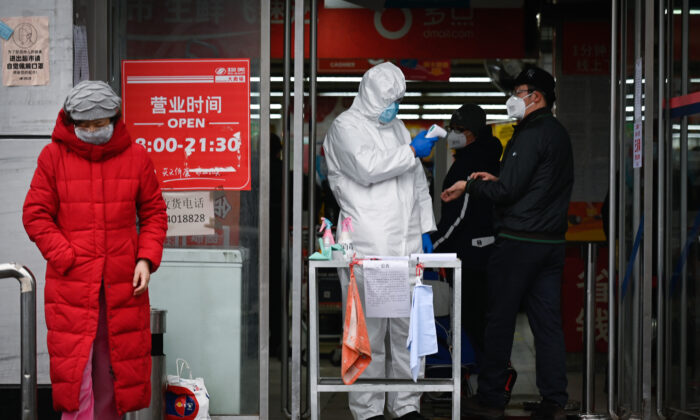 A staff member of a supermarket wearing a protective suit uses a thermometer to check the temperature of customers at the entrance of a supermarket in Beijing on Feb. 29, 2020. (STR/AFP via Getty Images)
