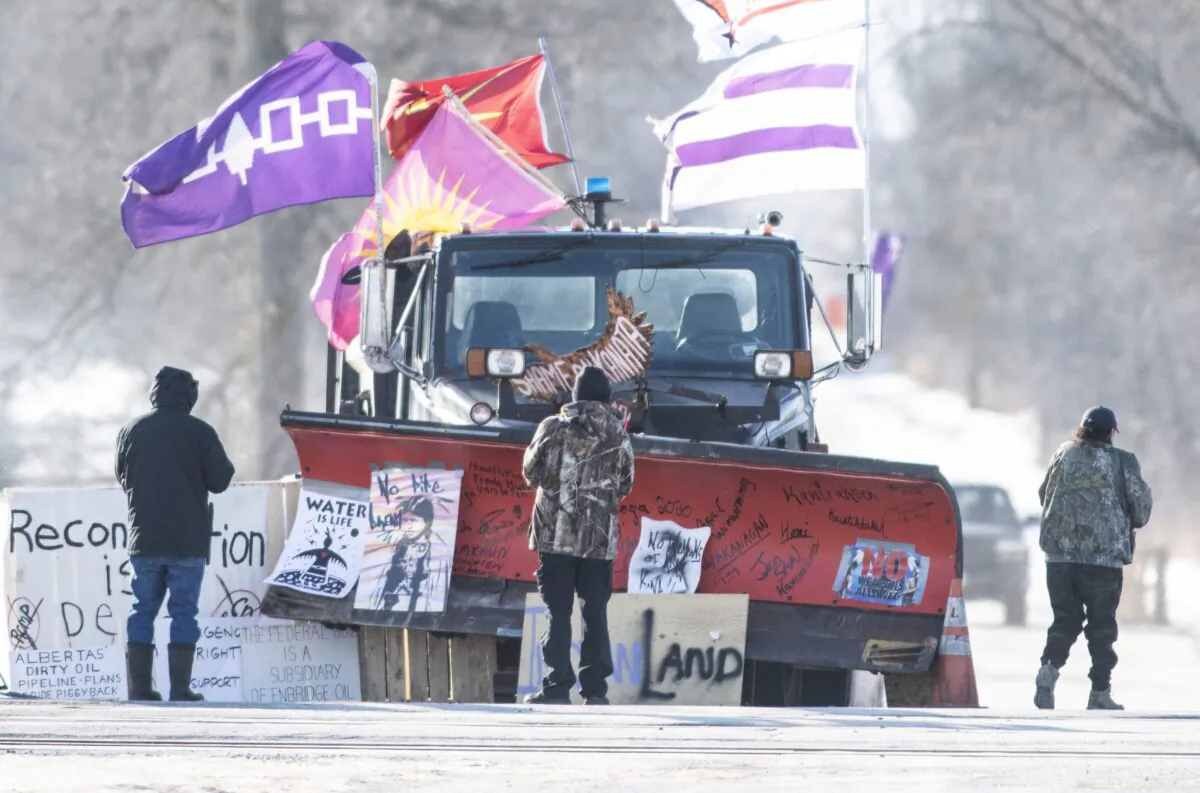Protesters look at signatures written on the blade of a snowplow parked adjacent to the closed rail line near Belleville, Ont., in Tyendinaga Mohawk Territory, on Feb. 20, 2020. (The Canadian Press/Justin Tang)