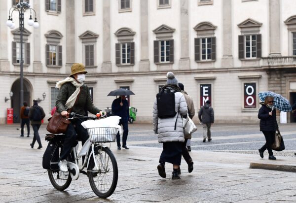 A woman wearing a protective mask crosses Piazza Duomo with her bicycle in Milan