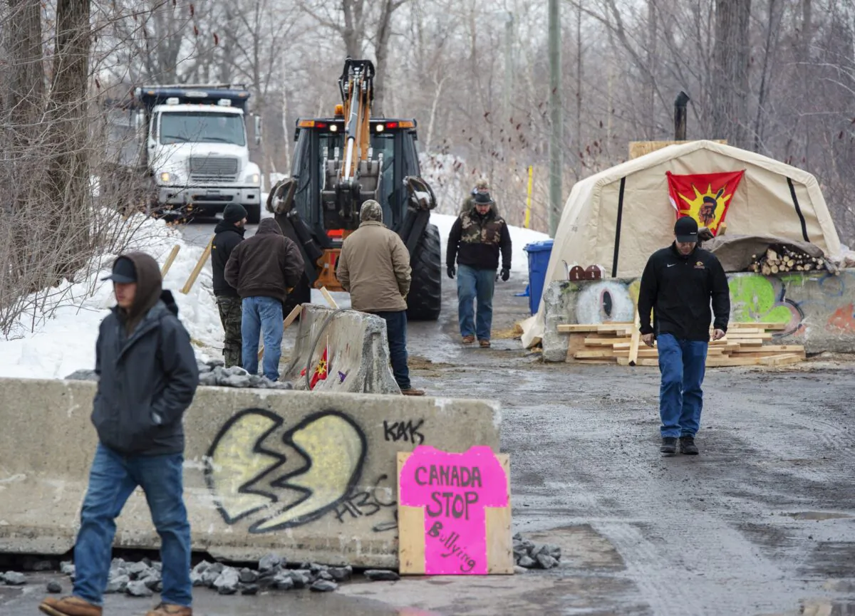 Members of the Mohawk community dump more gravel at the entrance to the blockade of the commuter rail line in Kahnawake, Que., on Feb. 26, 2020. (The Canadian Press/Ryan Remiorz)