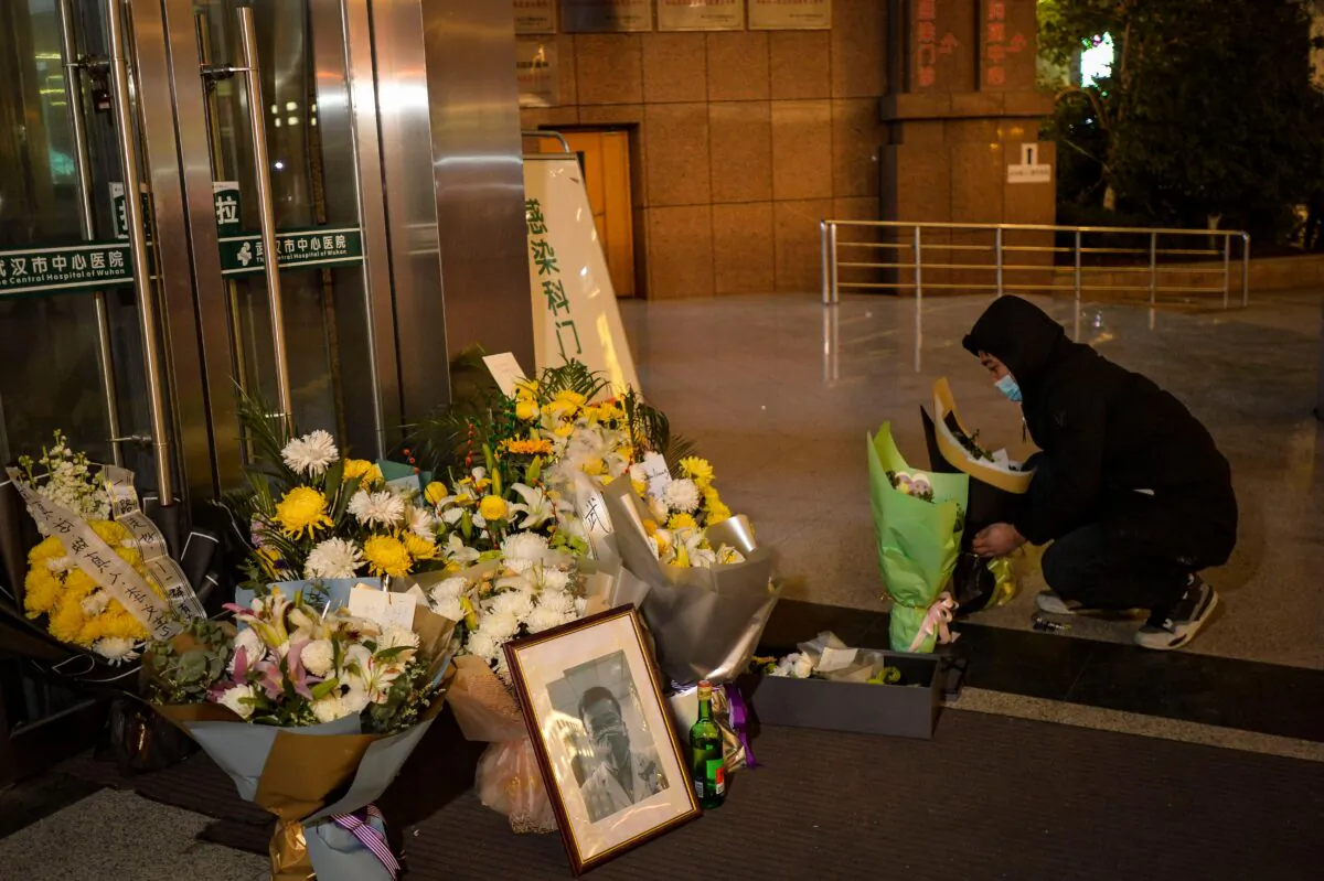 A man is placing flowers beside a photo of the late ophthalmologist Li Wenliang outside the Wuhan Central Hospital in Wuhan, China, on Feb. 7, 2020. (STR/AFP via Getty Images)