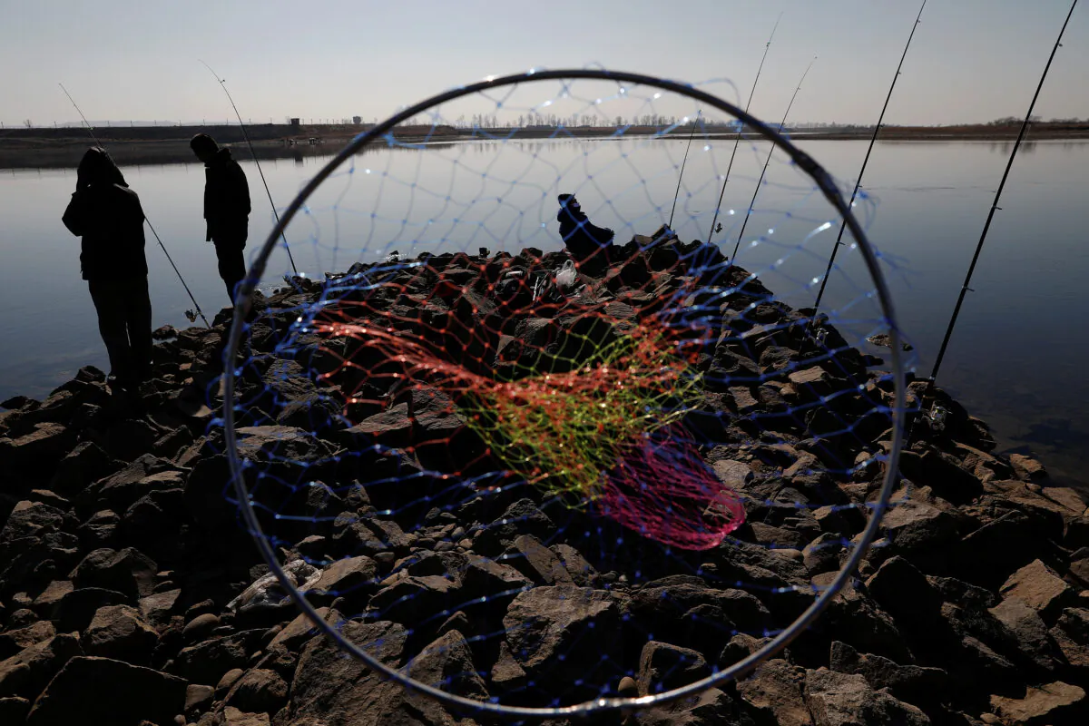 Chinese men fish as watchtowers are seen on the North Korean side of the Yalu River just north of Dandong, in China's Liaoning Province, on Nov. 20, 2017. (Damir Sagolj/Reuters)