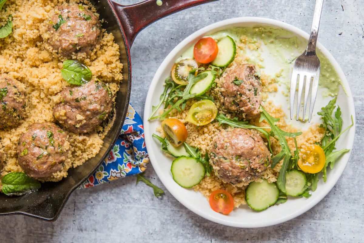 A generous swipe of whipped feta preps the plate for the rest of the meal: couscous, meatballs and crisp veggies, and plenty of fresh herbs. (Caroline Chambers)