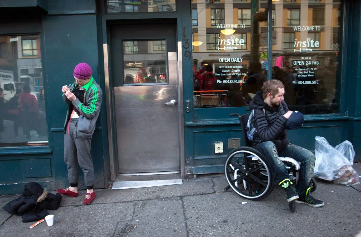 A woman prepares to inject herself with an unknown substance as a man sits in a wheelchair outside Insite, the supervised drug consumption site in Vancouver’s Downtown Eastside on Feb. 21, 2017. (The Canadian Press/Darryl Dyck)