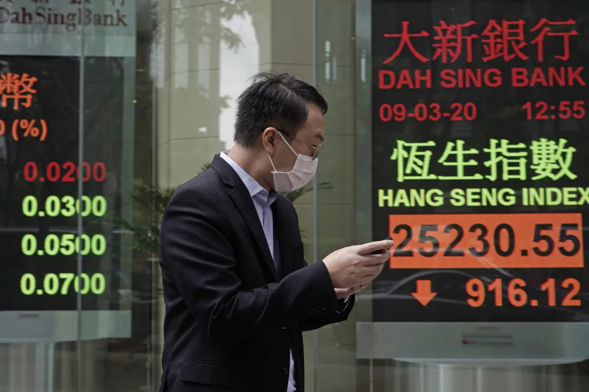 A man walks past an electronic board showing Hong Kong share index outside a local bank in Hong Kong, on March 9, 2020. (Kin Cheung/AP Photo)