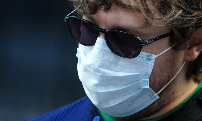 A man wearing a mask to protect against coronavirus takes pictures at the New York Stock exchange (NYSE) in the Manhattan borough of New York City, New York on March 9, 2020. (Carlo Allegri/Reuters)
